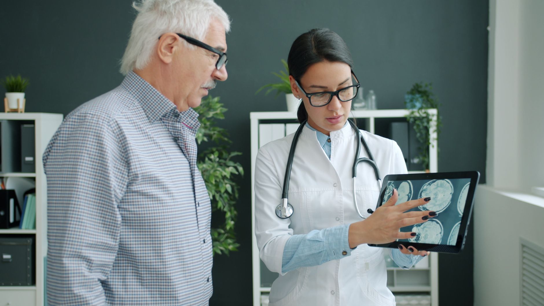 A clinician reviewing brain scans on a tablet with an older patient