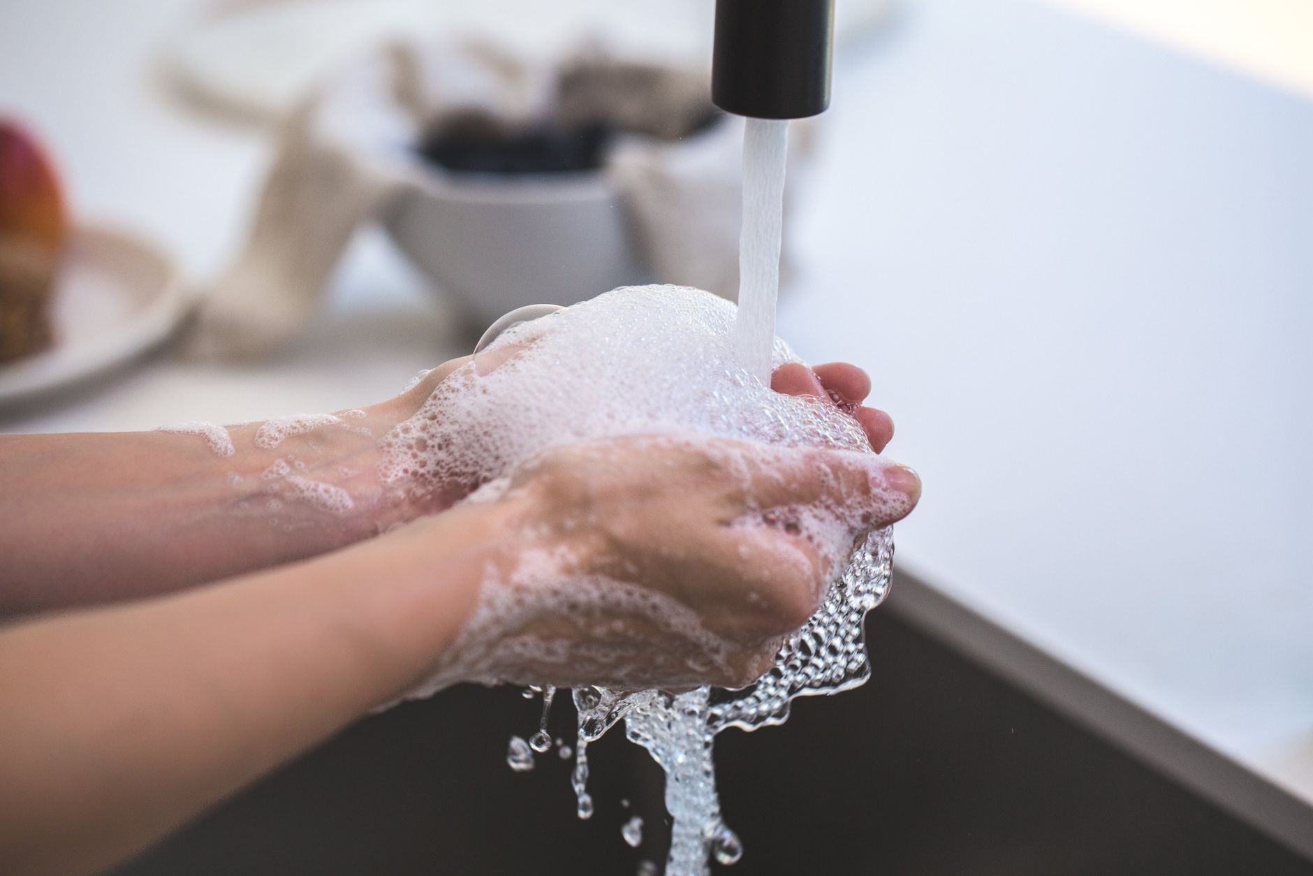 A pair of hands being washed under a running tap